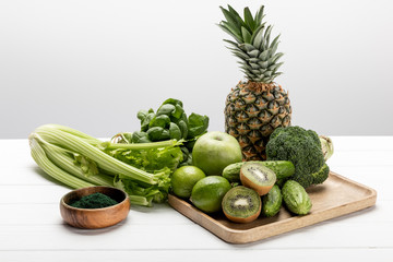 tasty pineapple, apple and limes near organic and raw vegetables on white