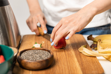 cropped view of woman cutting organic strawberry on chopping board near bananas on white