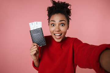 Excited young african woman posing isolated over pink wall background take selfie by camera with passport and tickets.