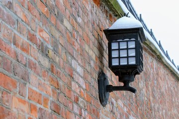 Street lamp hanging on a red brick wall. Close-up of a black vintage lantern covered with snow....