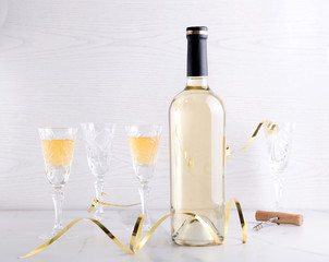 Party time. Bottle of white wine and wine glasses, holiday decor on the white table against light...