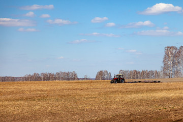 Fototapeta premium Red tractor with a trailed plow for mowing and weeding fields for the agro-industry of yellow color under the blue sky, a clear spring day. Preparation for planting crops rural technology. Farming.