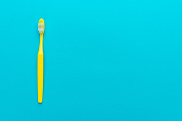 top view of plastic toothbrush on the blue background. minimalist flat lay photo of yellow toothbrush over turquoise blue background with copy space