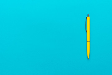 top view of ballpoint pen on the blue background. minimalist flat lay photo of yellow pen over turquoise blue background with copy space