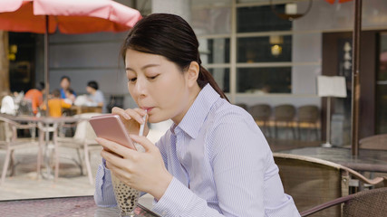 woman leadership drink pearl milk tea through straw in glass cup sitting outdoor cafe smiling laughing chatting online message on mobile phone. lady worker having afternoon tea time break from work.