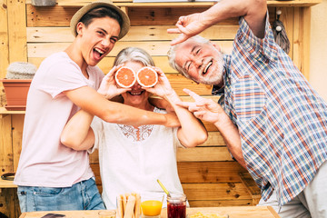 Senior couple grandparents with teenager nephew having fun at breakfast. Craziness and laughs. Wood on background and on table.Three people enjoying life. Food and drink - obrazy, fototapety, plakaty