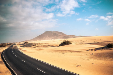 Fototapeta na wymiar Travel on the road concept with long way asphalt road in the middle of the dunes sandy desert and mountains for adventure and alternative scenic places for vacation or adventure lifestyle experience