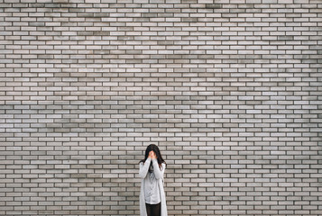 Beautiful young woman on the gray bricks background with sad expression covering her face with hands while crying. Depression and nwanted pregnancy concept. Copy space.