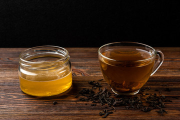 Cup of black tea and honey on dark wooden background.