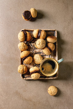 Baci di dama homemade italian hazelnut biscuits cookies with chocolate cream served in ceramic tray with cup of espresso coffee over brown texture background. Flat lay, space