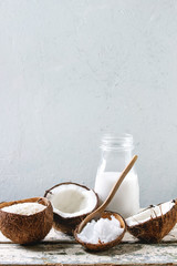Variety of coconut products milk in glass bottle, oil and flakes in shell, fresh broken coconut on old wooden table with grey wall at background. Healthy eating, copy space