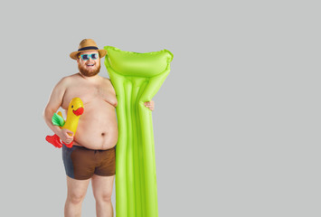 Fat funny man in swimming trunks with an inflatable mattress on a gray background.