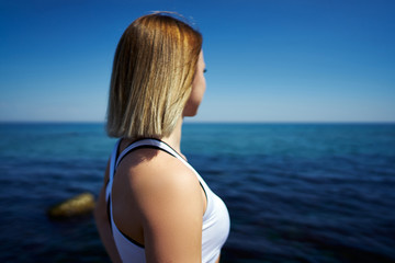 Fototapeta na wymiar Back view of a beautiful girl who looks into the sea or ocean on a sunny day.
