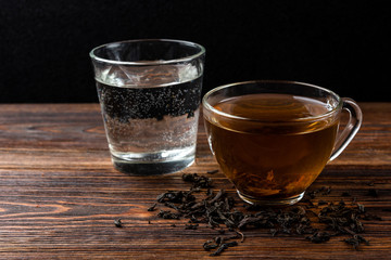 Cup of black tea and water on dark wooden background.