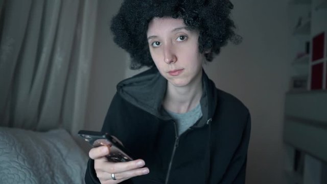 Afro haired white girl e mailed, chat with her smart phone and smiling to camera in her room. Curly haired happy woman slow motion video