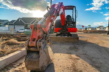 Close up of a red excavator with an attched grader blade viewed on a sunny day © Jason