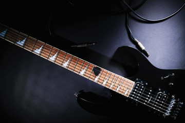 Modern black electric guitar with jack cable on black background