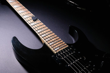 Body and neck of black electric guitar. Close up detail. On dark background