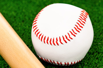 Close-up of wooden bat and baseball ball on artificial green grass