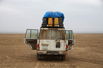 stojący samochód terenowy z otwartymi drzwiami podczas postoju na pustkowiu w pustynnym terenie - obrazy, fototapety, plakaty