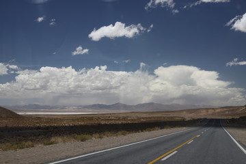 asfaltowa droga prowadząca do wielkiej solnej równiny w argentynie z andami i niebem w tle - obrazy, fototapety, plakaty