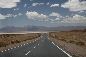 asfaltowa droga prowadząca do wielkiej solnej równiny w argentynie z andami i niebem w tle - obrazy, fototapety, plakaty