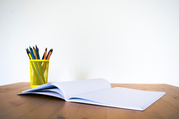 Fototapeta premium Notebook and glass with pencils and pens on a wooden table. Front view