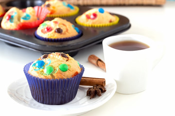 Homemade lemon muffins with colorful chocolate candy in paper case and cup tea. White background. Selective focus.