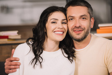 happy man hugging attractive and cheerful woman at home