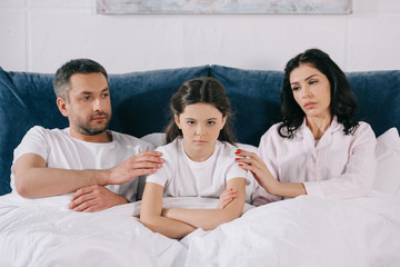 Obraz premium worried parents touching upset kid with crossed arms in bedroom