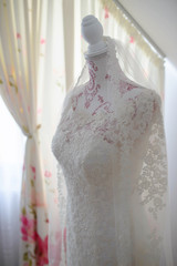 Gorgeous classic wedding dress with transparent embroidered lace corset set on a vintage mannequin torso or a dress form against a bright window, an unique vestimentary piece for the bride-to-be
