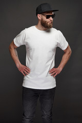 Hipster handsome male model with beard wearing white blank t-shirt and a baseball cap with space for your logo or design in casual urban style