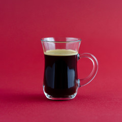 Transparent cup of black coffee placed on a red surface.