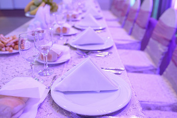 Sitting arrangement at a fine dining restaurant or party venue, with purple artificial light elements, and table setup with white china, linen napkins, glassware and silverware in the order of use