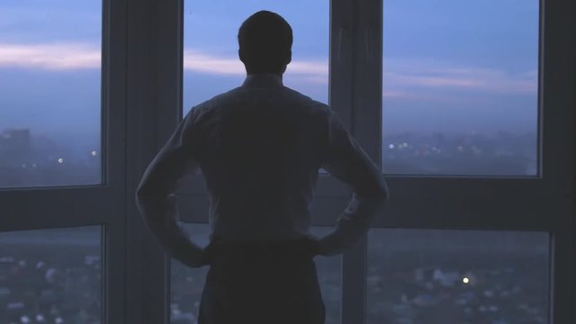 Back view of a businessman stands near the window and looks on night city background. 3840x2160