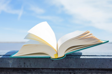 An open green book lies on a background of blue sky. The concept of summer reading, outdoor recreation with a book. Bright sunny day.