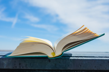 An open green book lies on a background of blue sky. The concept of summer reading, outdoor recreation with a book. Bright sunny day.