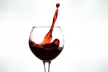 Red wine splash into glass on white background
