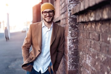 Portrait of stylish handsome young man in glasses with bristle standing outdoors. Man wearing...