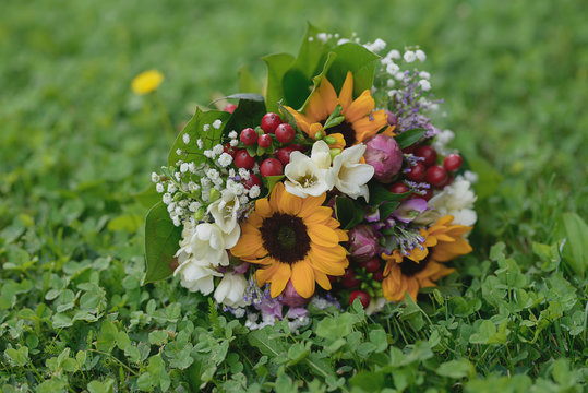 Sunflowers, freesias and berries floral arrangement set on green, fresh grass. Rustic wedding bouquet for the bride or bridesmaids or florist ideas for bridal and ceremonial flower arrangements.