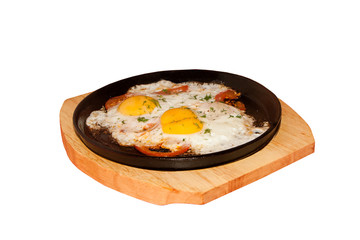 fried eggs roasted with tomatoes on the frying pan standing on a wooden support.