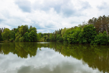 Landscape with cloudy sky, Cumulus clouds, green forest and lake with reflections in the water after the rain in spring
