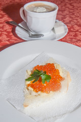 red caviar sandwich and mug from a cappuccino on a table in cafe.