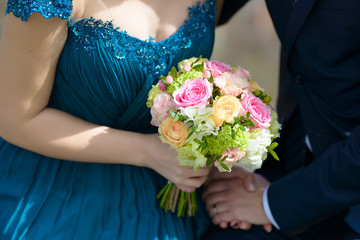 Bride wearing a blue dress and groom at the wedding with focus on bride's hands holding a large round bouquet featuring pastel colored roses, traditional floral arrangement and accessory for the bride