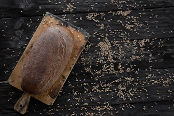whole grain bread is lying on a wooden table. Wheat grains are scattered nearby.