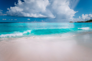 Beautiful white wave rolling towards tropical sandy beach. Gorgeous fluffy clouds above blue sea. Seychelles Grand Anse, La Digue, Seychelles