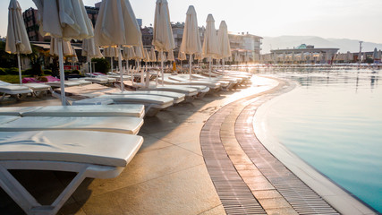 Toned image of empty sun bed at poolside at early morning. Nobody at swimming pool. Empty summer beach hotel resort
