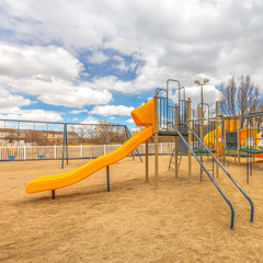 Square Playground with slides and swings under the blue sky filled with puffy clouds