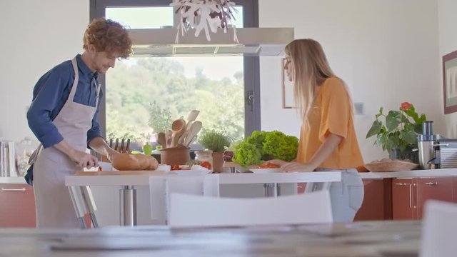 Young people couple cooking and preparing food for lunch or dinner at home open space kitchen. Mediterranean healthy diet vegetables,tomatoes,salad. Modern love relationship,helping.4k video