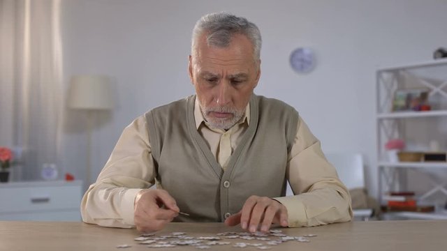 Old man exercises with puzzle, suffers cognitive impairment, Alzheimer symptom